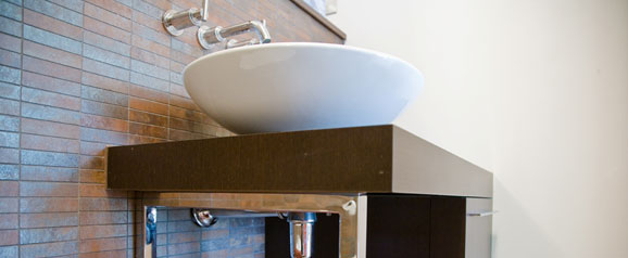 A wash basin in a teenage boys’ en-suite bathroom, using wenge dark wood cabinetry to compliment the earthy metallic mosaic tiles.